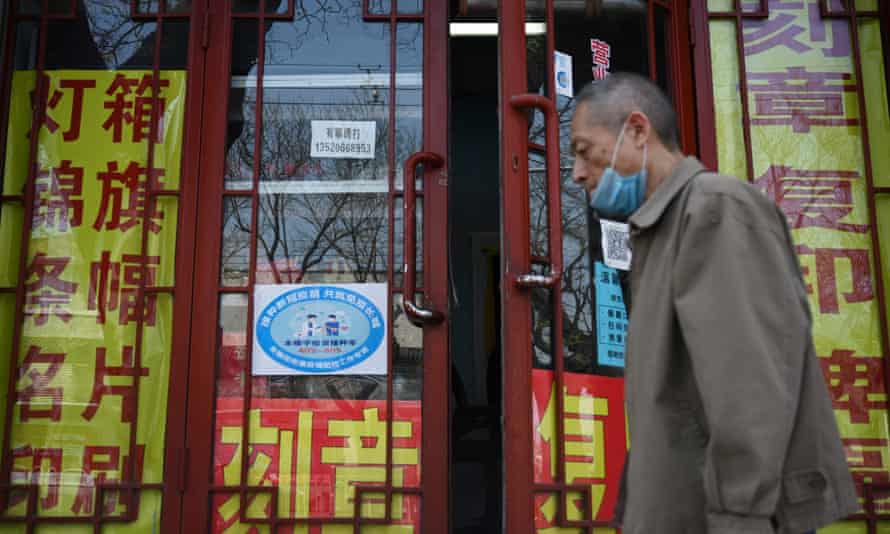 A man walks past a blue sign indicating workers’ Covid vaccination rates on the door of a printing business in Beijing.