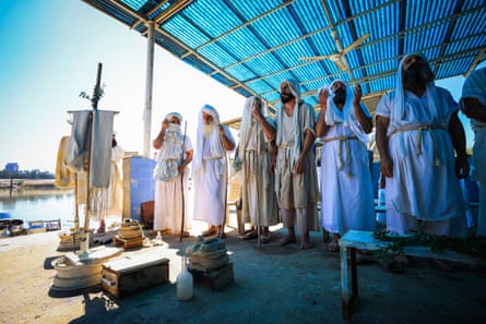 A group of people wearing white garments stand outside by water.