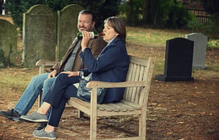 Ricky Gervais and Penelope Wilson sit on a bench in a graveyard, she drinking out of a bottle