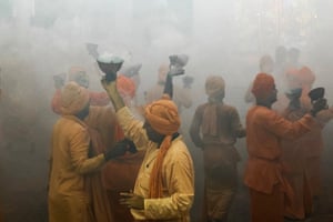 Smoke envelops people wearing yellow and orange as they hold aloft incense burners