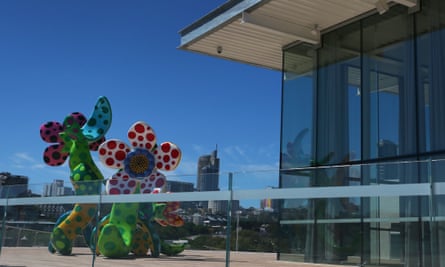 Large flower sculpture sits on an outdoor deck in front of floor to ceiling glass windows