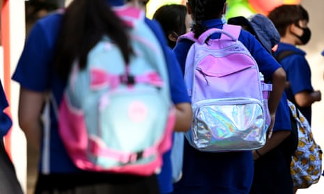 A rear view of primary school children walking to class with backpacks