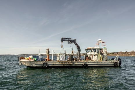 Two men stand on a fishing boat with a crane on its deck, not far from the shore