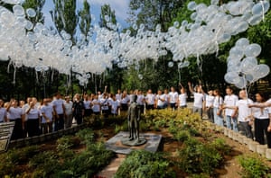 A crowd of people release white balloons while standing around a statue of two children