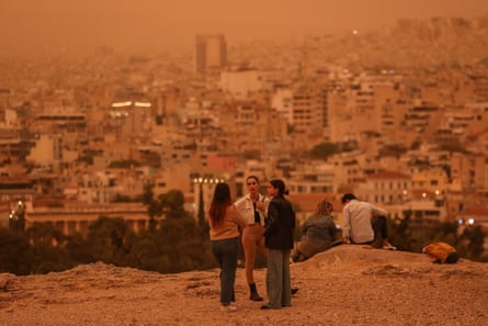 People stroll around the Acropolis area while an orange haze covers the sky