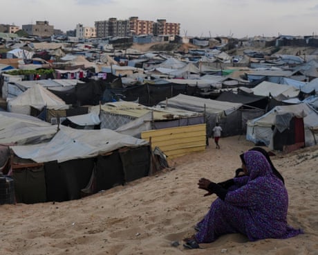 Two women sit in front of a large tent camp