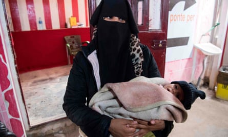 A Syrian woman holding a child waits at a makeshift clinic at al-Hawl