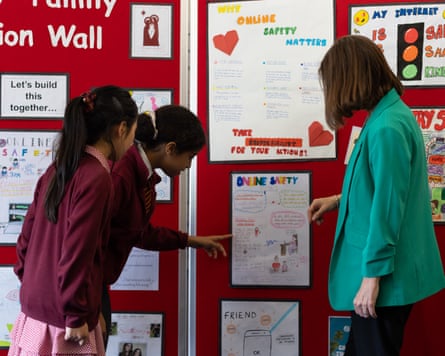 Two pupils and Yvonne Rutherford, the school’s deputy headteacher, look at a display board in the school with posters about online safety