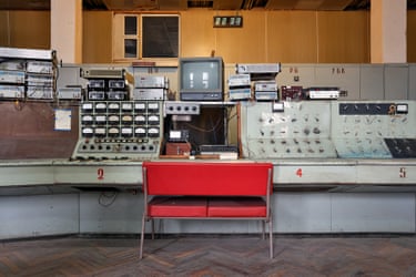A red two-seat chair in front of a run-down control panel