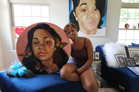 woman leans on painting of breonna taylor while sitting on bed or sofa. another painting of taylor hangs in background