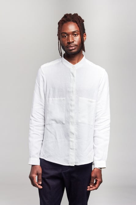 A male model in a white linen shirt standing against a grey background.
