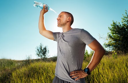 Young man is refreshing himself with water from a bottle after a workout in nature