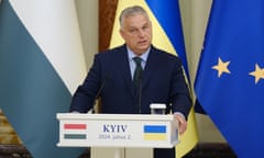 Viktor Orbán speaking in Kyiv: he is behind a lectern with the Hungarian and Ukrainian flags depicted on its front and more flags, including the EU flag of gold stars on dark blue, are seen behind him