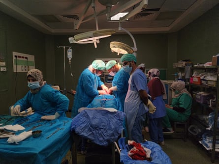 Six medical workers in a small operating theatre.