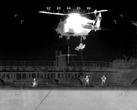 Soldiers rappell from a helicopter on to the deck of a ship at night