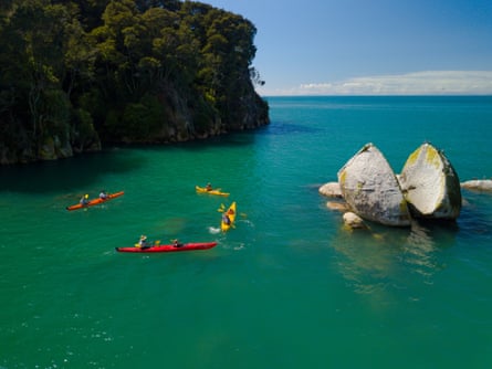Kayakers paddle near a giant round boulder that has broken in half