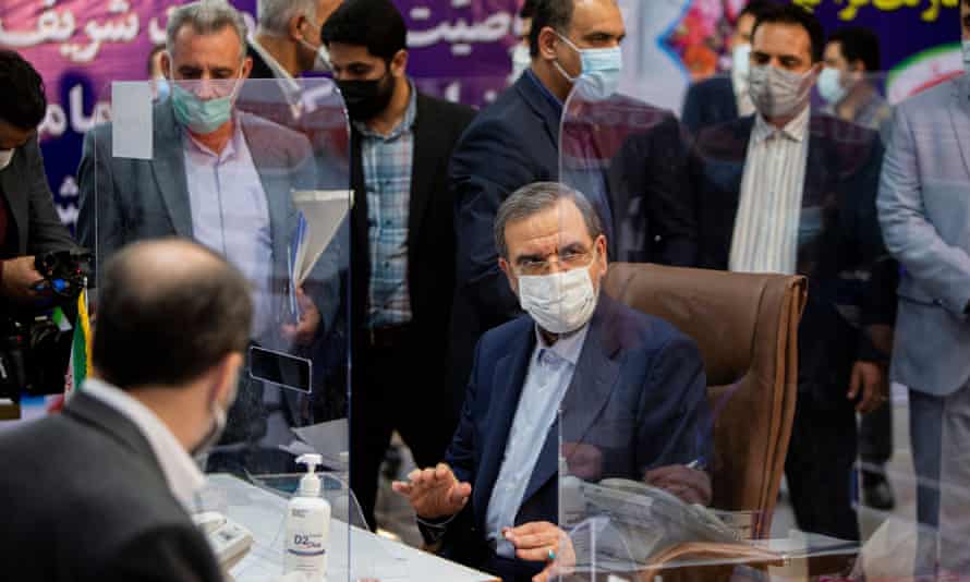 man in face mask sitting at a desk surrounded by other people in masks behind transparent partitions