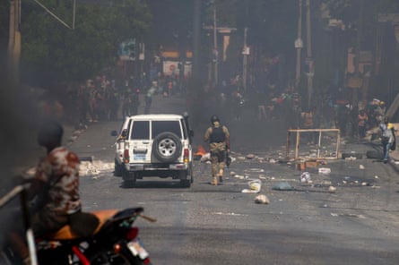 Smoke from a burning barricade rises as an armed police officer walks near protesters making their way to the Villa d’Accueil to demand increased security from the government, in Port-au-Prince on 2 April.