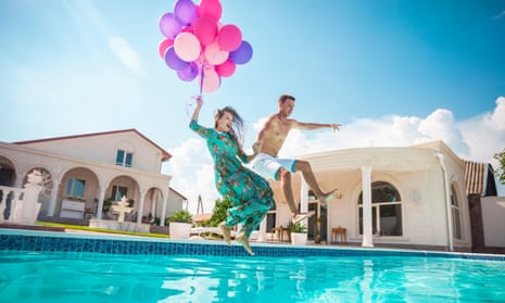 Happy young couple jumping into the pool while holding a bunch of balloons