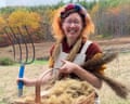 Eve Ogden Schaub smiles, holding a pitchfork beside a basket of flax fiber she grew