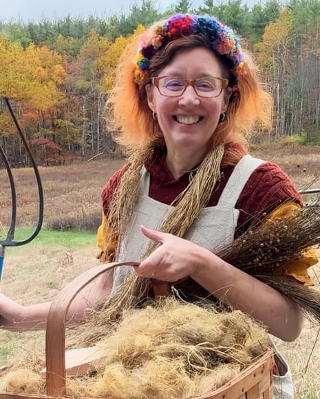 Eve Ogden Schaub smiles, holding a pitchfork beside a basket of flax fiber she grew