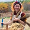Eve Ogden Schaub smiles, holding a pitchfork beside a basket of flax fiber she grew
