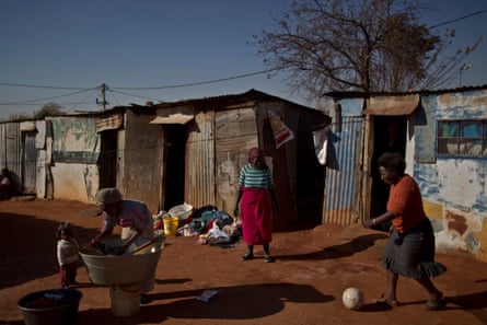 A woman washes her laundry while others play with a football next to their homes in Soweto township on the outskirts of Johannesburg, South Africa.