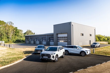 Chery, Omoda and Jaecoo crossover models parked on tarmac in front of a grey industrial building with garages.