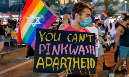 A man with a mask during Covid holds a sign reading “You can’t pinkwash apartheid”, with a rainbow flag with a star of David on it, during the 2020 Pride parade in Tel Aviv