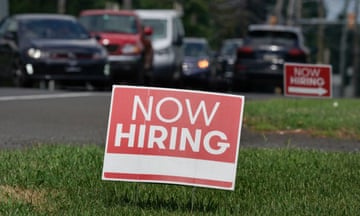 A red 'Now Hiring' sign sits on grass