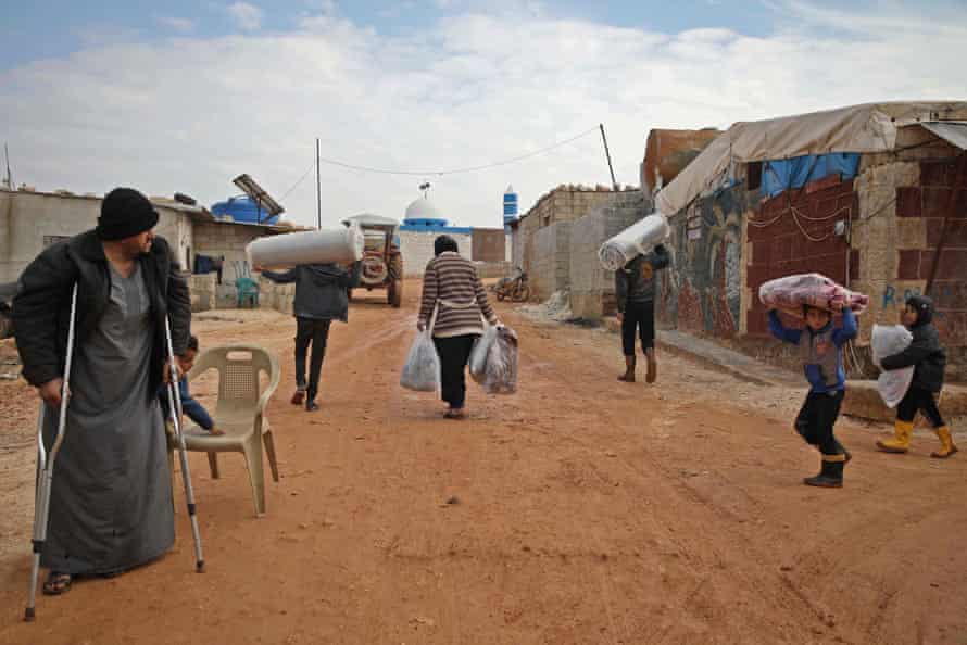 People carry blankets and mattresses at Atma camp