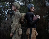 Two men stand back to back outside, one in a military uniform and the other in a football uniform carrying a ball