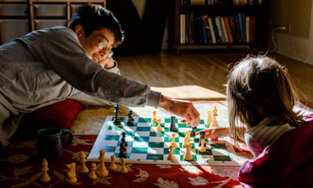 A smiling Dad lays on floor with little girl playing chess in sunshineGettyImages-1226029058
