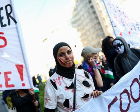 A young woman with a fake scar on her face and a holed T-shirt holding a banner