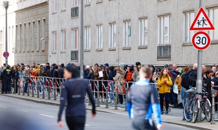A line of people on the pavement outside a grey building