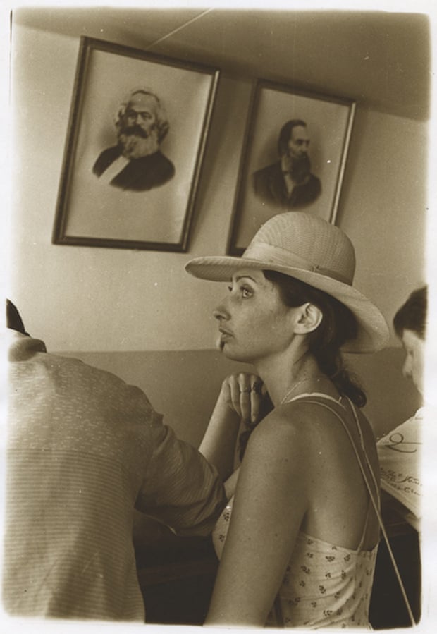 A woman in a sundress and straw hat in front of framed portraits of Karl Marx and Friedrich Engels