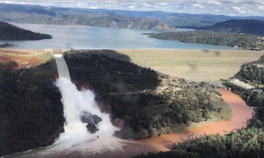 Water pours from an open spillway coming from a full lake with a dam.