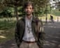 A young man with a beard in a white shirt and jacket with spectacles and a park behind him