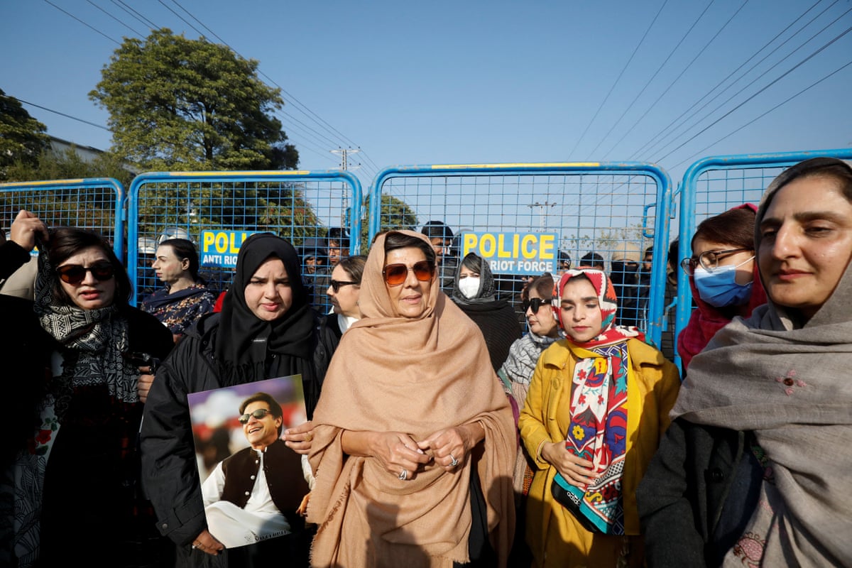 A woman in traditional Pakistani dress surrounded by supporters at a police barrier
