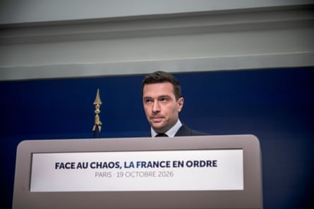 Bardella looks sideways behind a lectern reading “Face au chaos, la France en ordre”