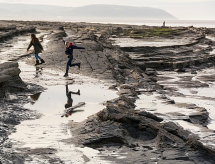 Children running on a rocky beach with headland in the distance