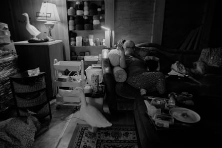 a woman reclines on a sofa crocheting at home, surrounded by yarn and a decorative goose figurine