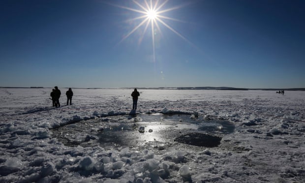 Les gens se tiennent devant ce qui aurait été le site d'impact d'un météore qui a explosé au-dessus de la ville russe de Tcheliabinsk en 2013.