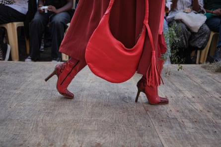 A red handbag is held next to red leather high heeled boots and a red coat.