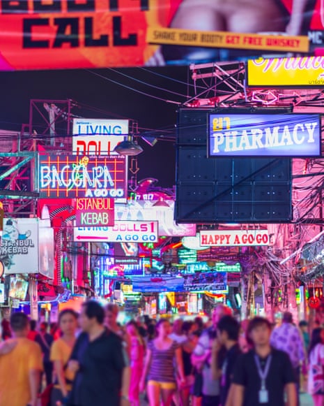 A crowded street at night lined with bright neon signs and illuminated storefronts