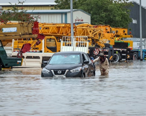 A man pushes his car past inundated vehicles on a flooded road in Dubai