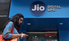 A woman checks her mobile phone as she walks past a mobile store of Reliance Industries’ Jio telecoms unit in Mumbai<br>FILE PHOTO: A woman checks her mobile phone as she walks past a mobile store of Reliance Industries’ Jio telecoms unit, in Mumbai, India
