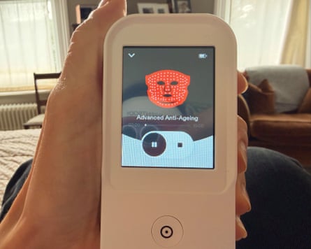 A hand holds a handheld LED device displaying a glowing red facial mask icon and âÂÂAdvanced Anti-Ageingâ text