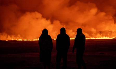 People watch as the night sky is illuminated by the eruption of a volcano near Grindavík.