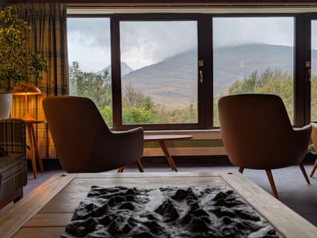 A lounge with two club chairs and large windows overlooking a landscape of mountains and trees